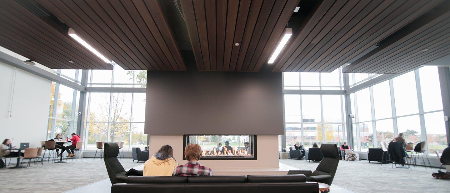 people seated on a couch looking towards a fireplace in the center of a large room