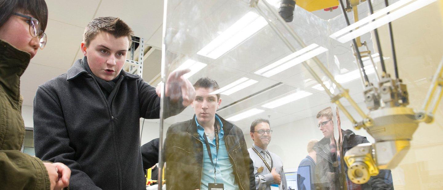 students pointing and looking at a machine in a glass case