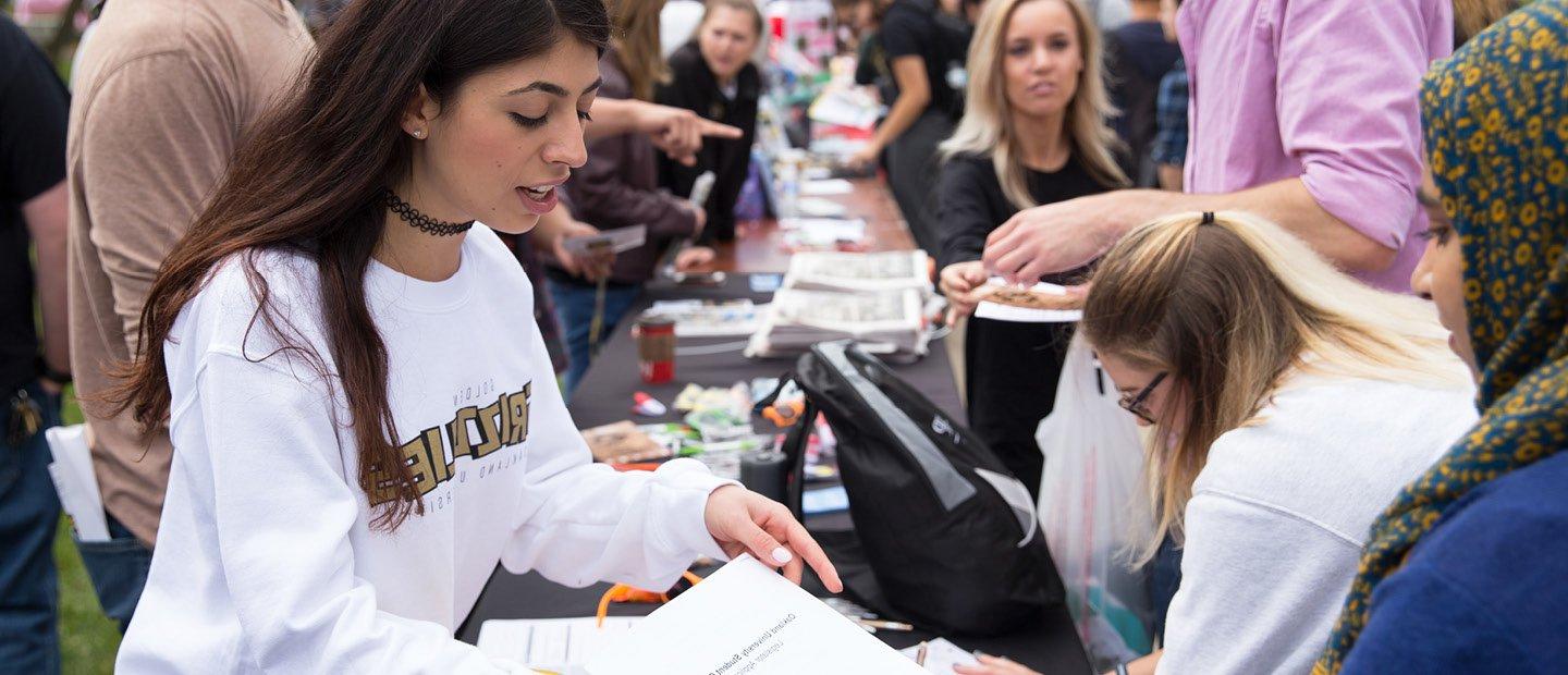 student handing a flyer to a woman at a student organization fair