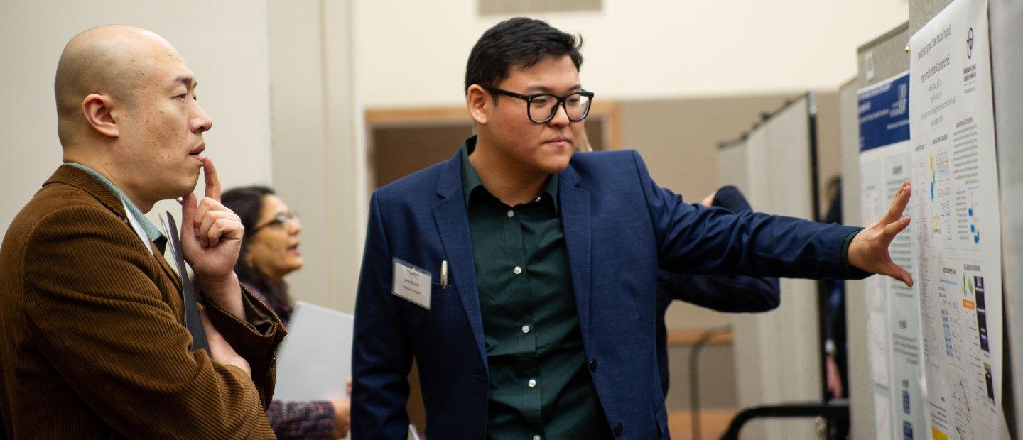 A faculty member presenting posters on a board to another faculty member.