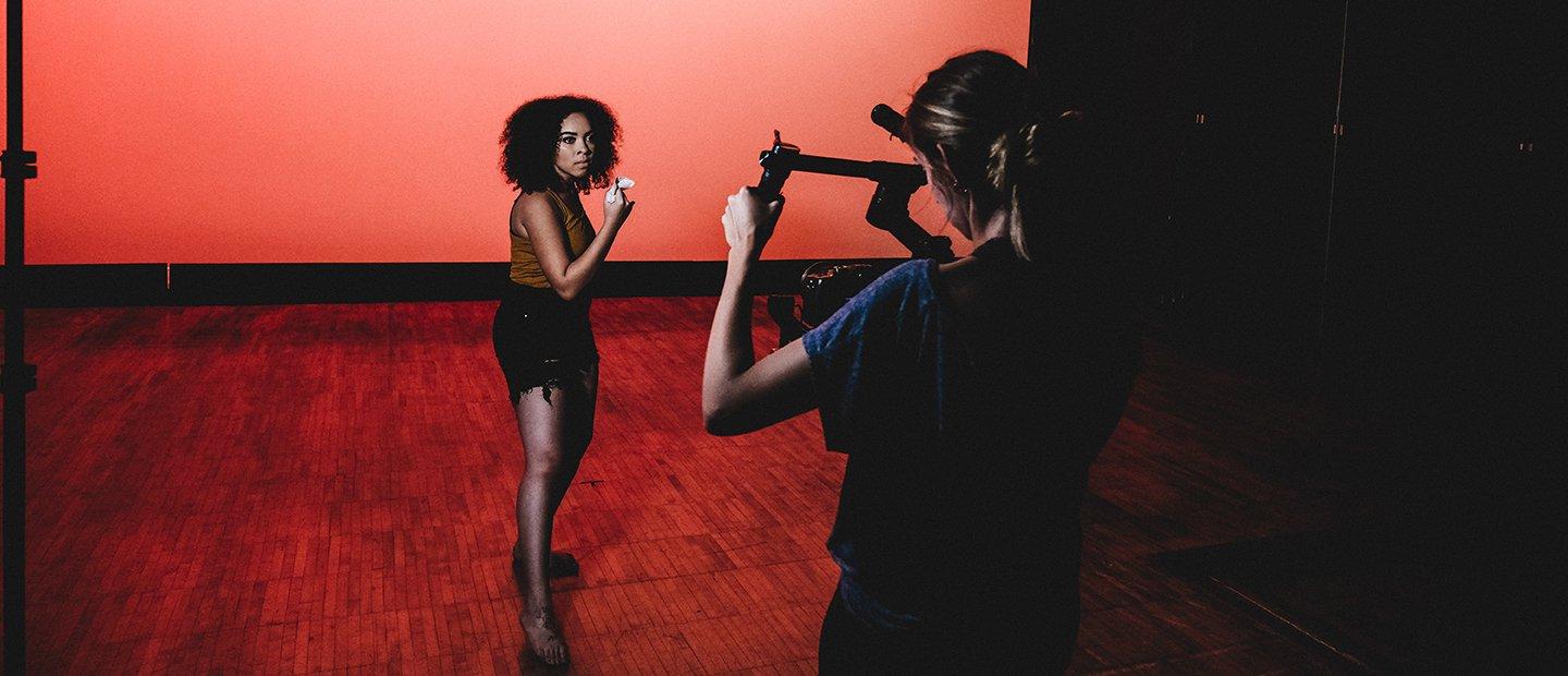 A young woman recording a performer on a stage with a red background.