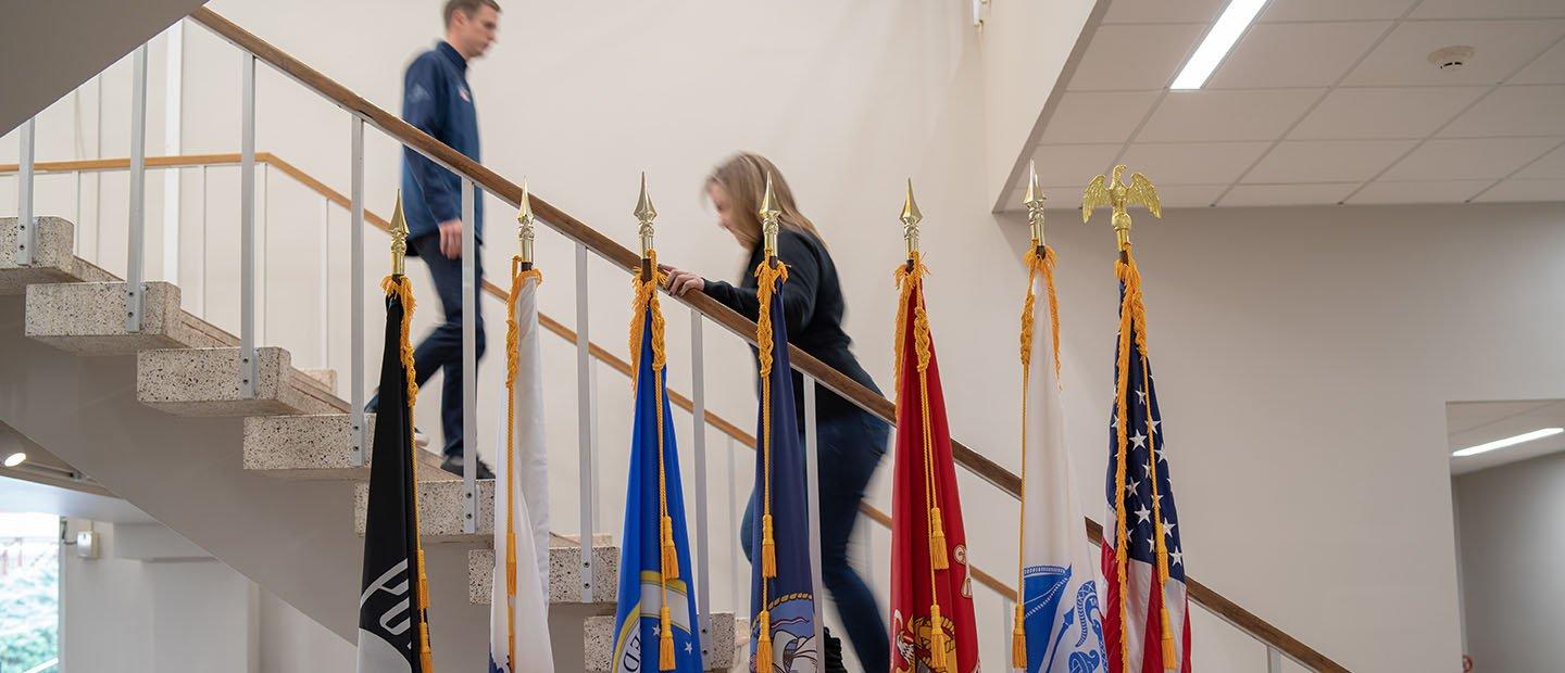 two people on a stairway behind a row of flags